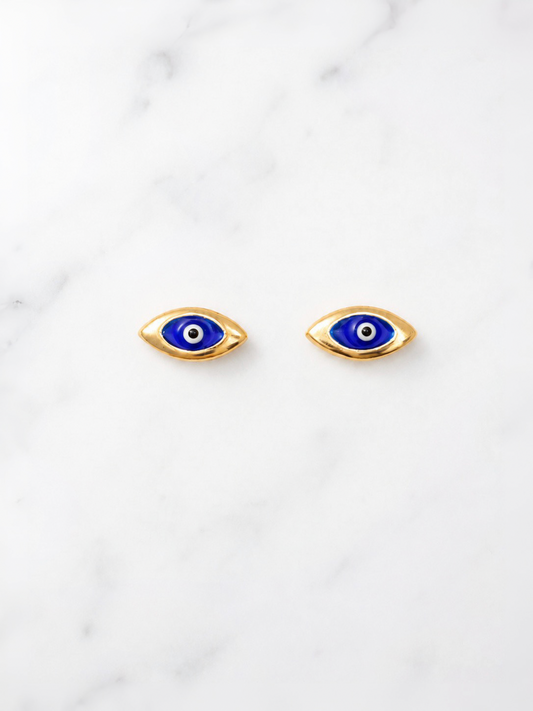 A pair of gold-toned evil eye stud earrings with blue, white, and black details, displayed on a white marble surface.