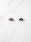 A pair of gold-toned evil eye stud earrings with blue, white, and black details, displayed on a white marble surface.