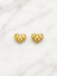 A pair of gold heart-shaped stud earrings with a textured, faceted diamond pattern and a beaded border, displayed on a white marble background.