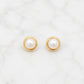 A pair of gold circular stud earrings with white pearl centers, displayed on a white marble surface.