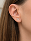 A close-up of a woman's ear wearing a small gold leaf stud earring with clear stones.