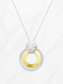 A modern pendant necklace featuring concentric silver rings with a textured gold center, topped with a textured silver disc, suspended from a delicate silver chain on a white marble background.