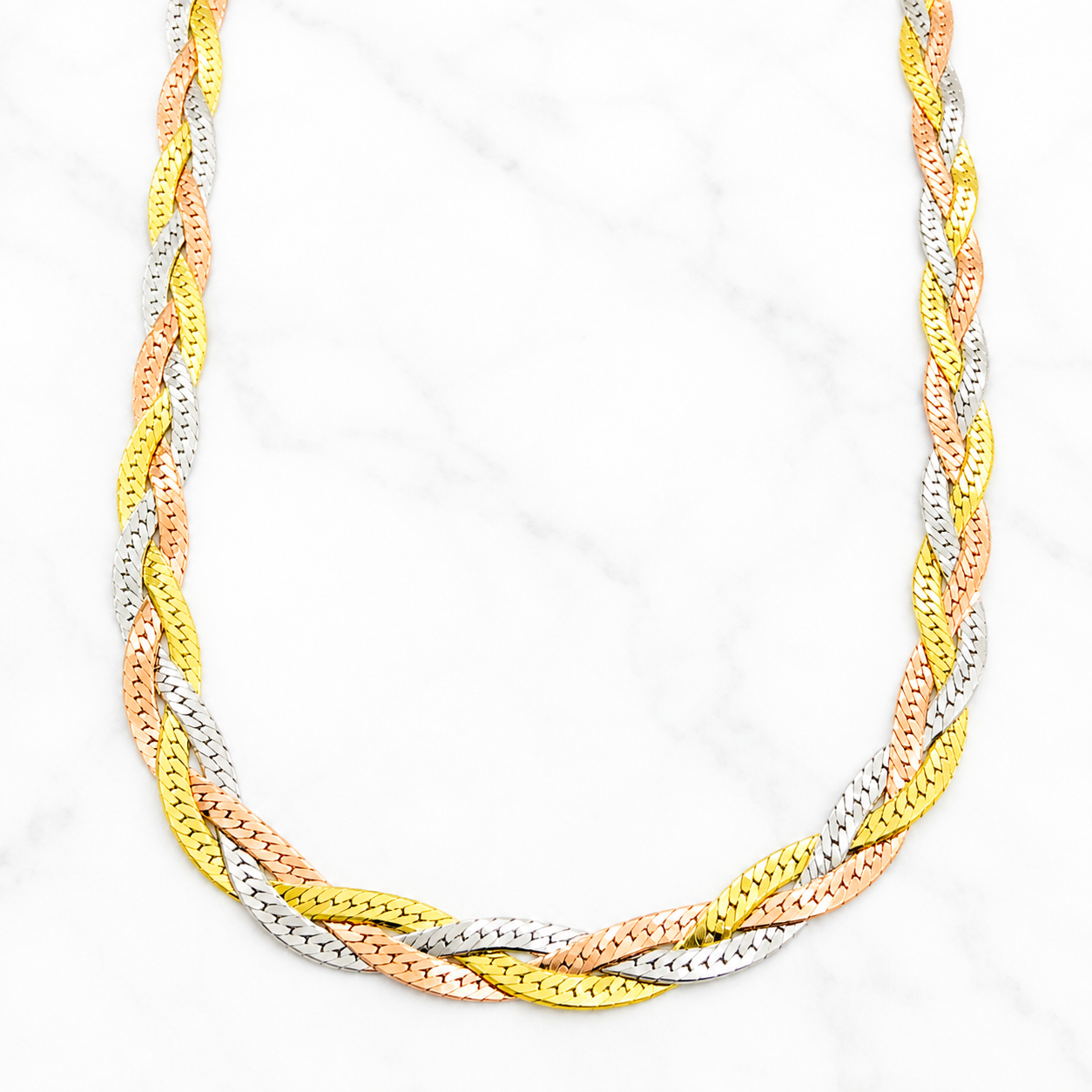 A three-tone braided chain necklace featuring interwoven yellow gold, silver, and rose gold links, displayed on a white marble background.