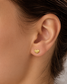 A close-up of a person's ear wearing a small textured gold heart stud earring.