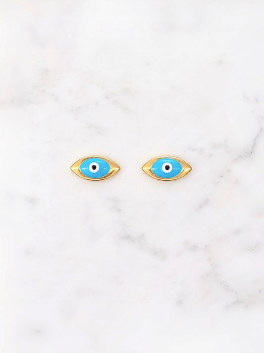 A pair of gold-tone evil eye stud earrings with bright blue enamel, white centers, and black pupils, displayed on a white marble surface.