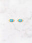 A pair of gold-tone evil eye stud earrings with bright blue enamel, white centers, and black pupils, displayed on a white marble surface.