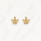 A pair of gold crown-shaped stud earrings set with small clear gemstones, displayed on a white marble surface.
