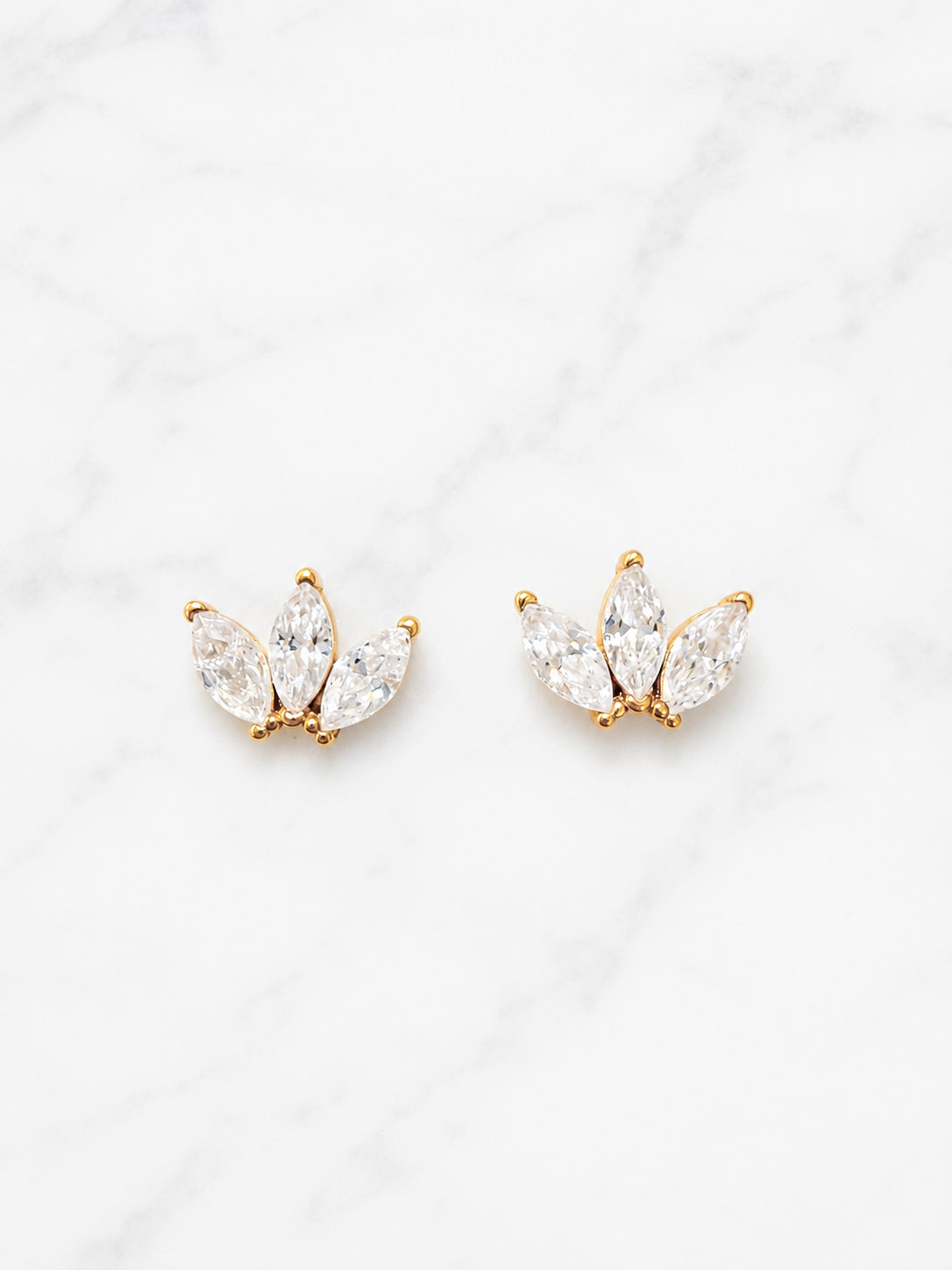 A pair of gold butterfly stud earrings with marquise-cut clear crystals, displayed on a white marble background.