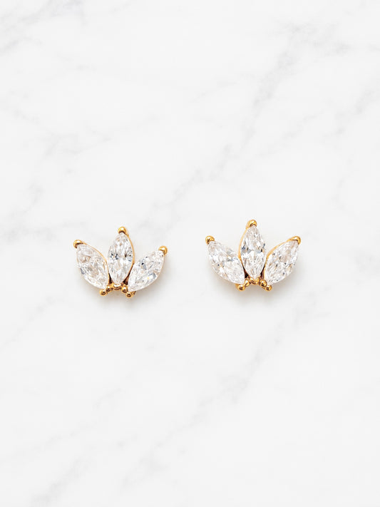 A pair of gold butterfly stud earrings with marquise-cut clear crystals, displayed on a white marble background.