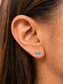 A close-up of a person's ear wearing a small evil eye stud earring with blue, white, and gold details.